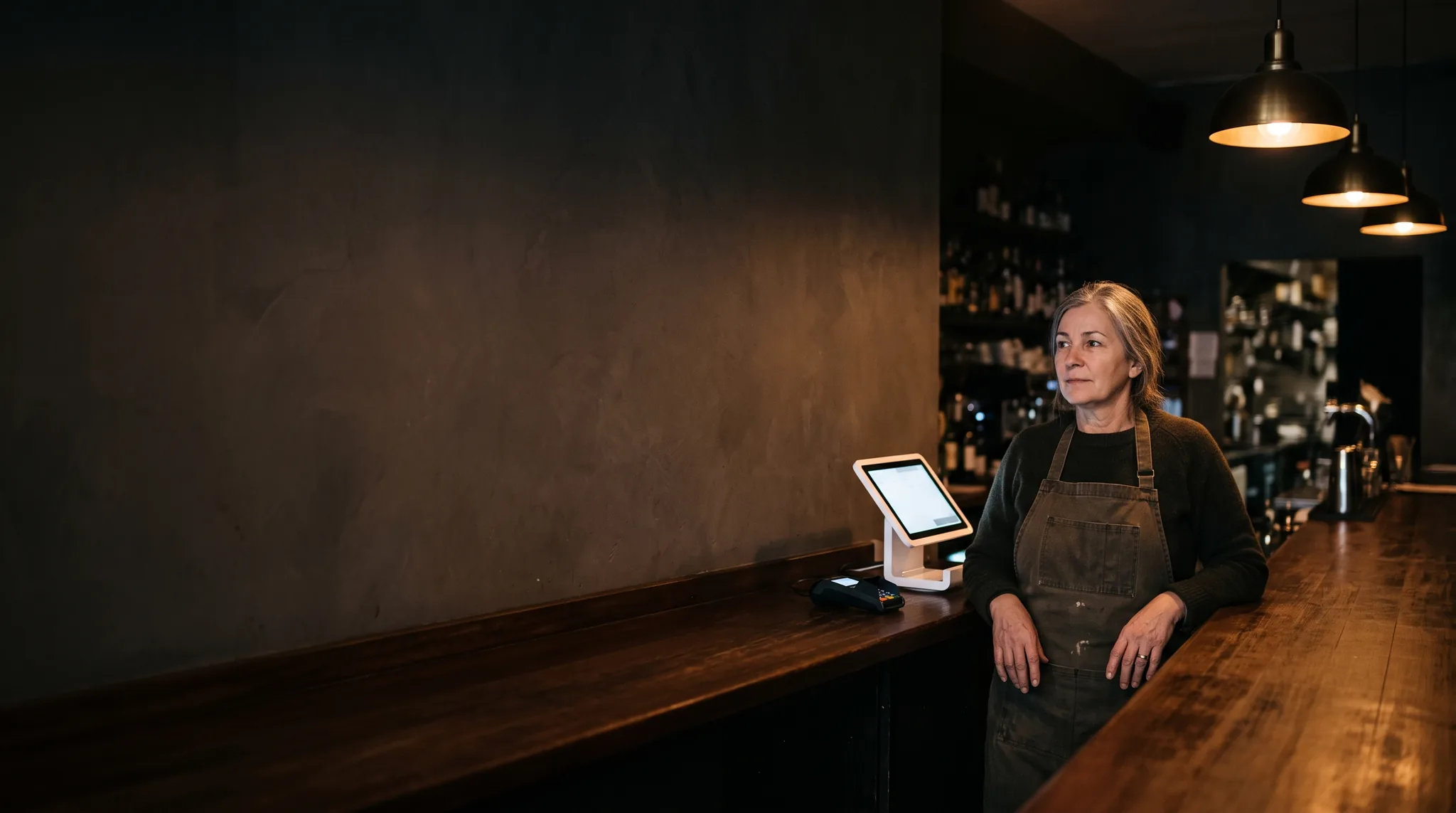 Bistro owner behind the bar beside a Genius touchscreen register and card reader
